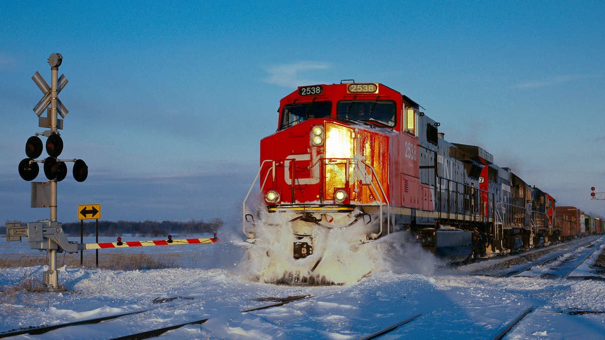 A photograph of a CN train at a rail grade crossing. There is snow on the ground.