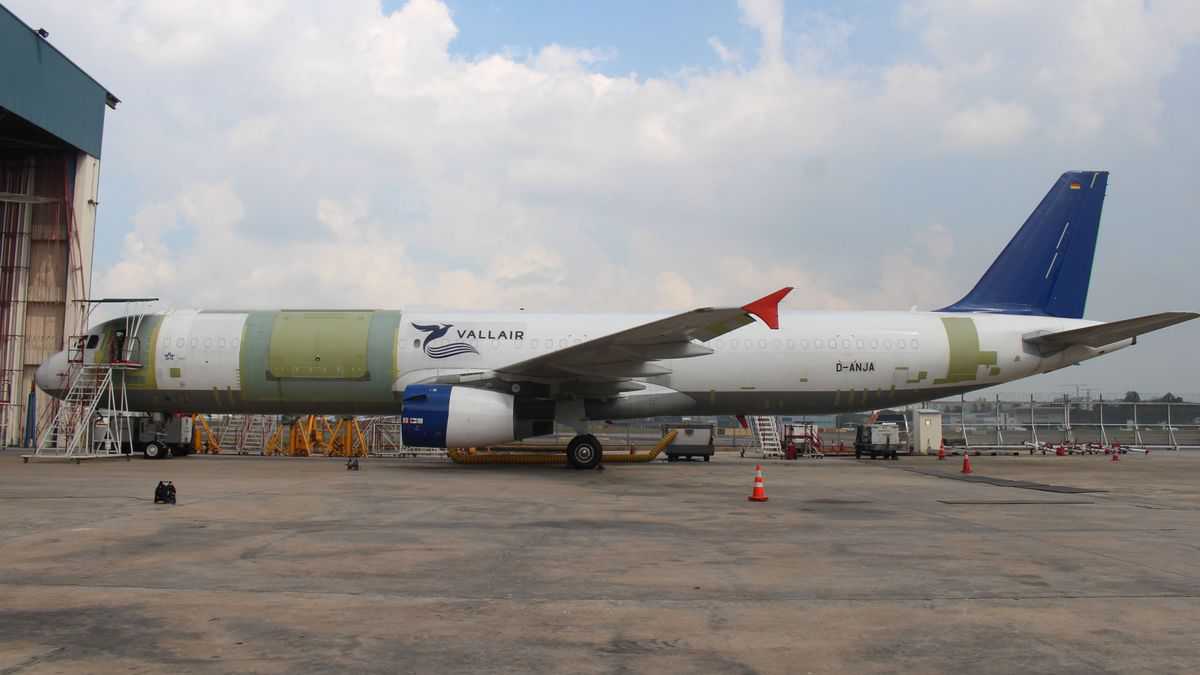 A plane sitting outside a hangar with patches on fuselage where modified doors and other changes are being made.