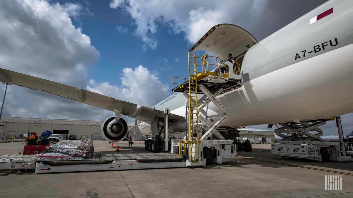 A gray and white jet gets loaded with cargo on a sunny day.