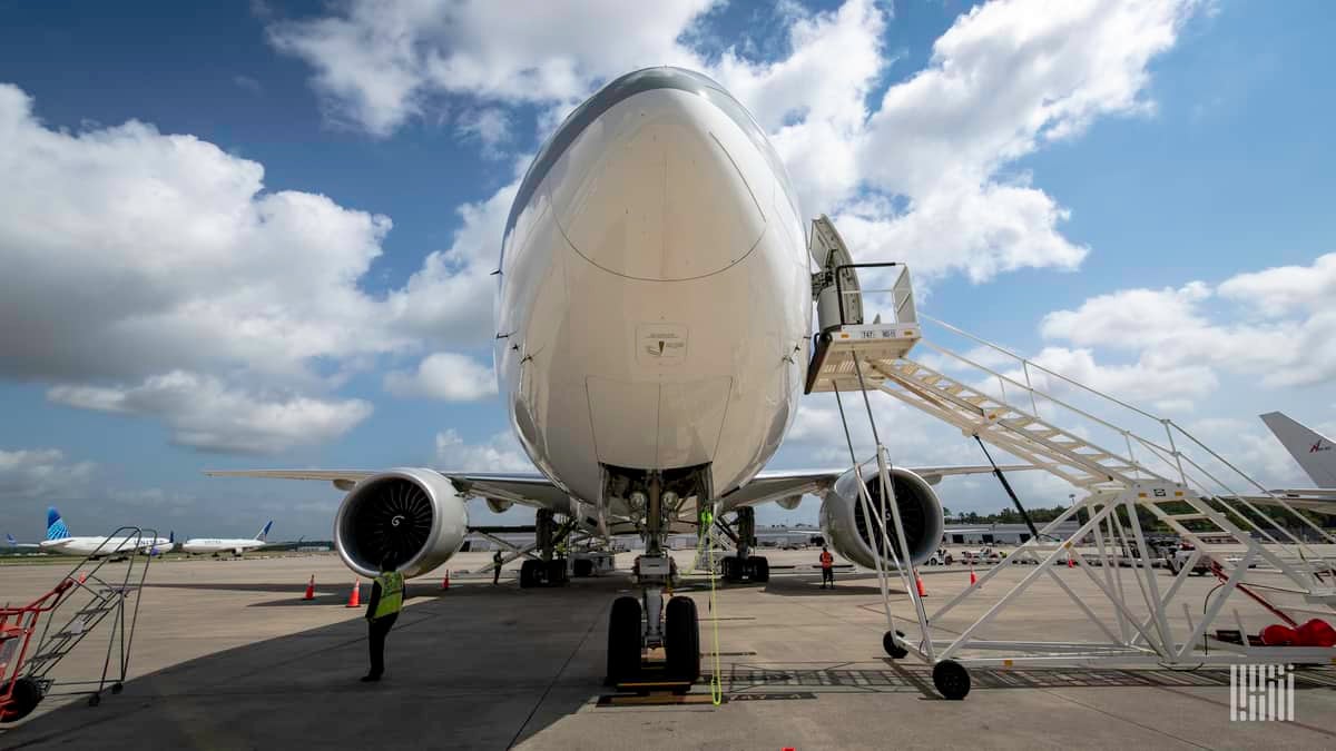 Staring staight at the nose of a 747 cargo jet under a bright sky with white clouds.