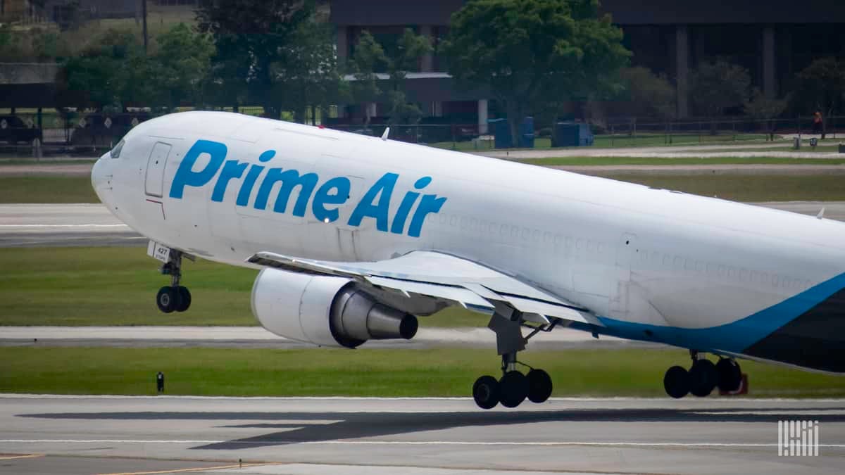 A white Amazon cargo jet with front wheel lifting off on takeoff.