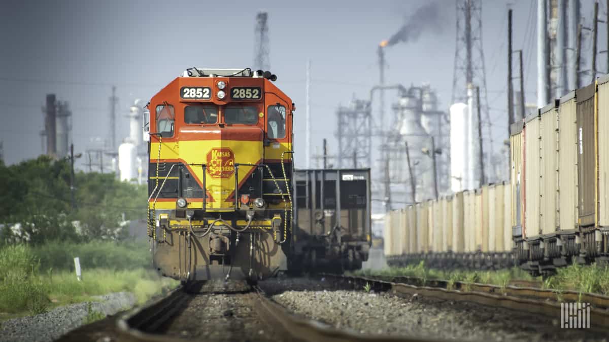 A photograph of a Kansas City Southern train traveling away from a city center.