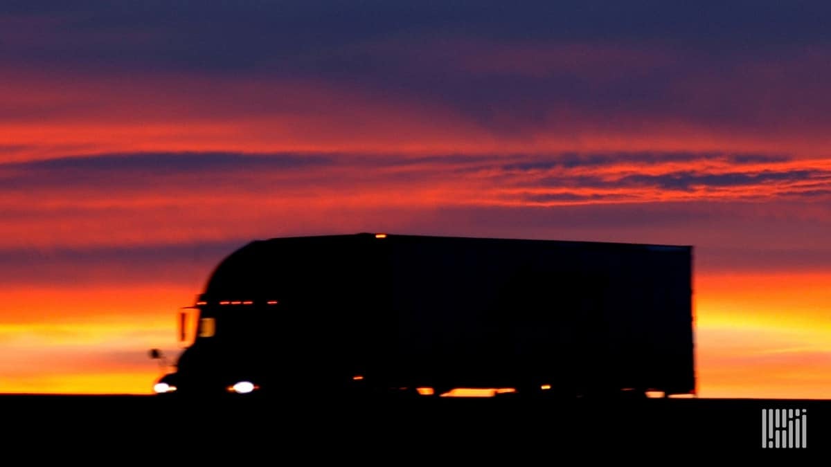 Sun on the horizon behind a tractor-trailer on a desert road.