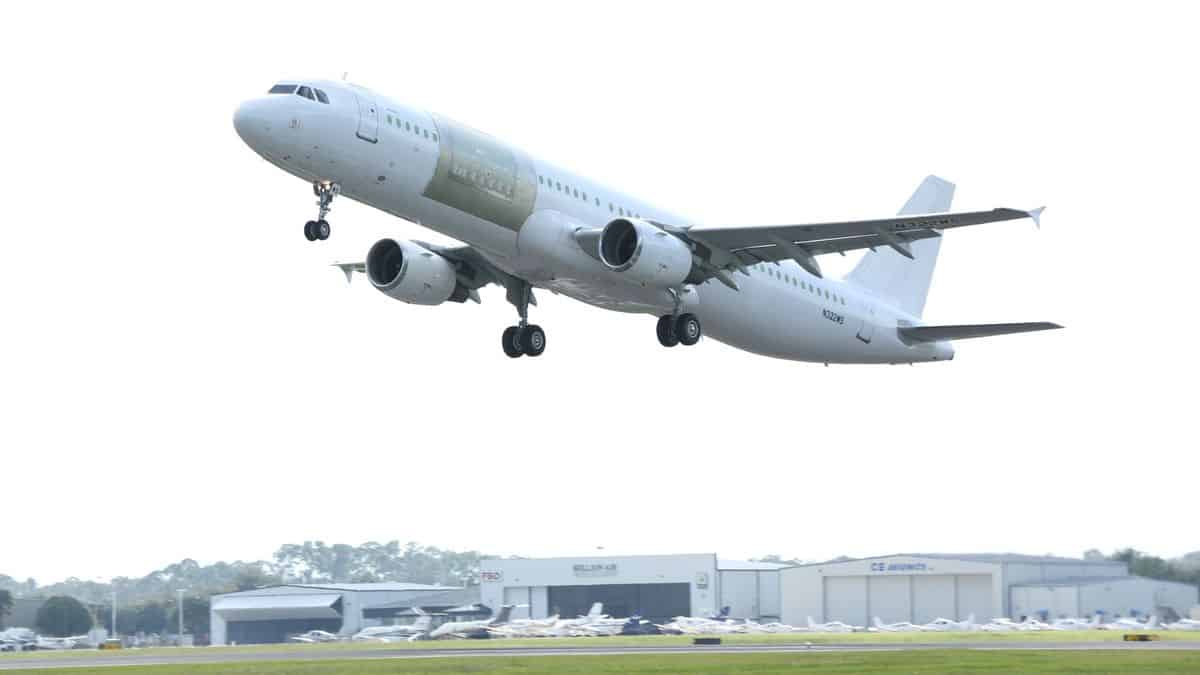 A plain white jet with a new cut-in cargo door outlined in frame takes off. It's an A321 converted freighter on its first test flight.