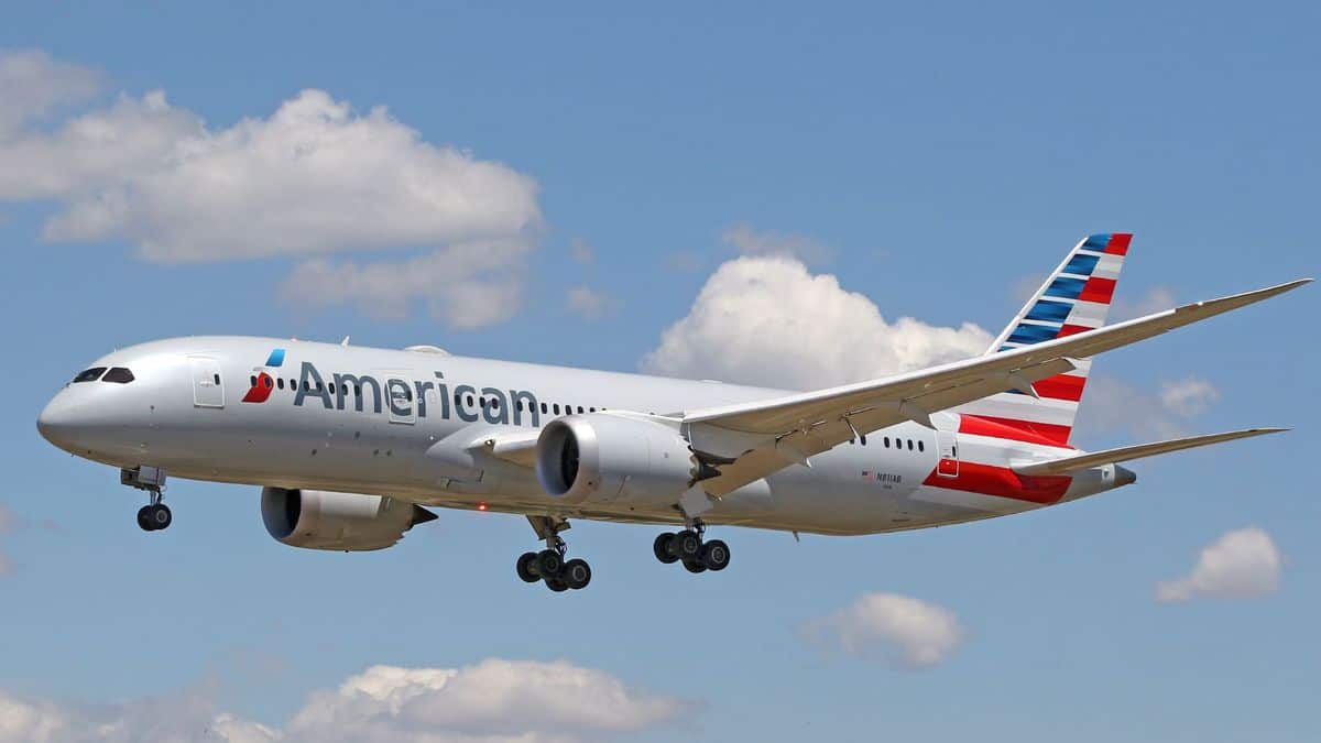 A light gray American Airlines jet comes in for landing on sunny day with wheels down.