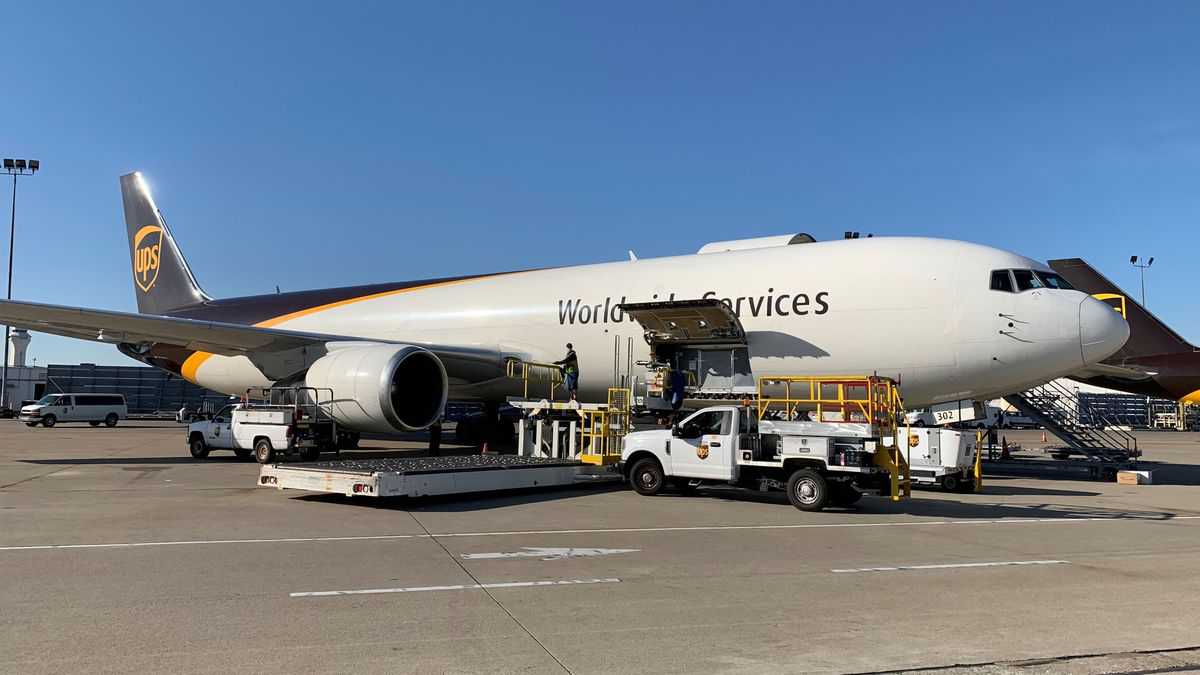 A white UPS plane with brown tail sits on ramp with cargo door open on side.