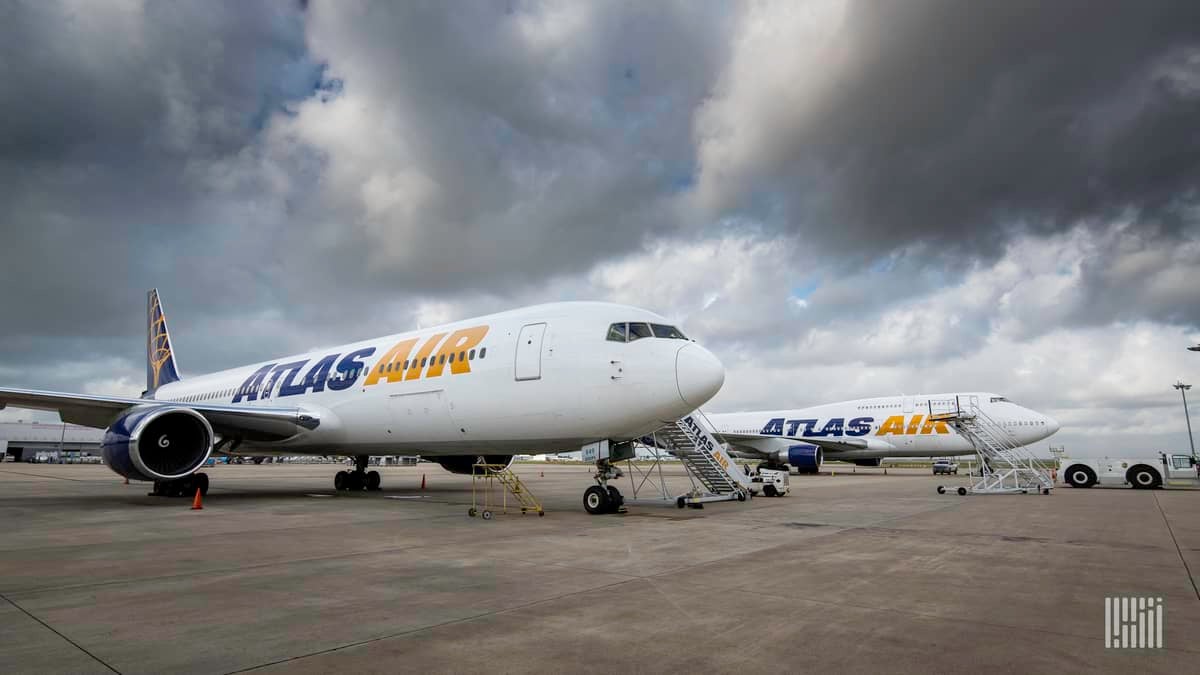 White jets with blue tails, parked at airport, with stormy skies looming.