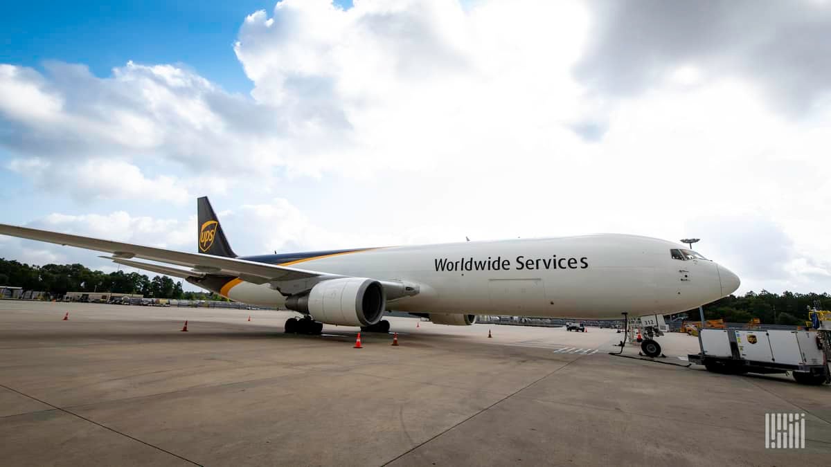 A white UPS jet with brown tail sits on ramp on sunny day.