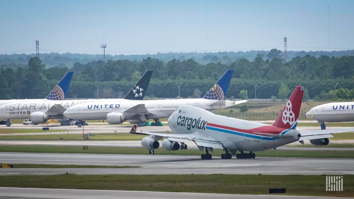 A jumbo jet lifts off the runway with several planes parked in the background.