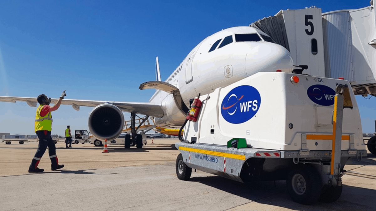 A ramp workers guides equipment preparing a plane for its next flight on a bright sunny day.