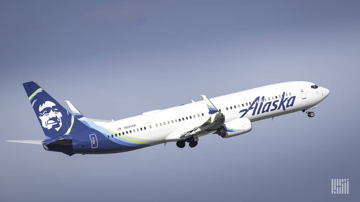 A white jet with blue tail and native Alaskan painted on tail, on ascent through the sky.