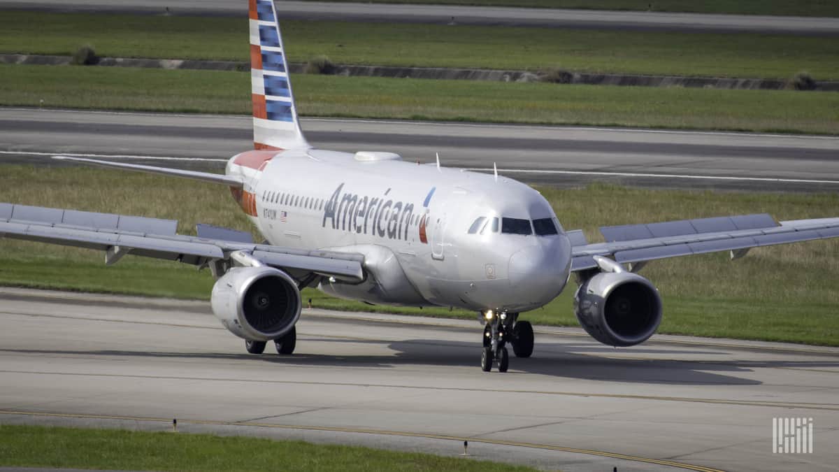 A silver American Airlines jet with flag-pained tail moves down taxiway.