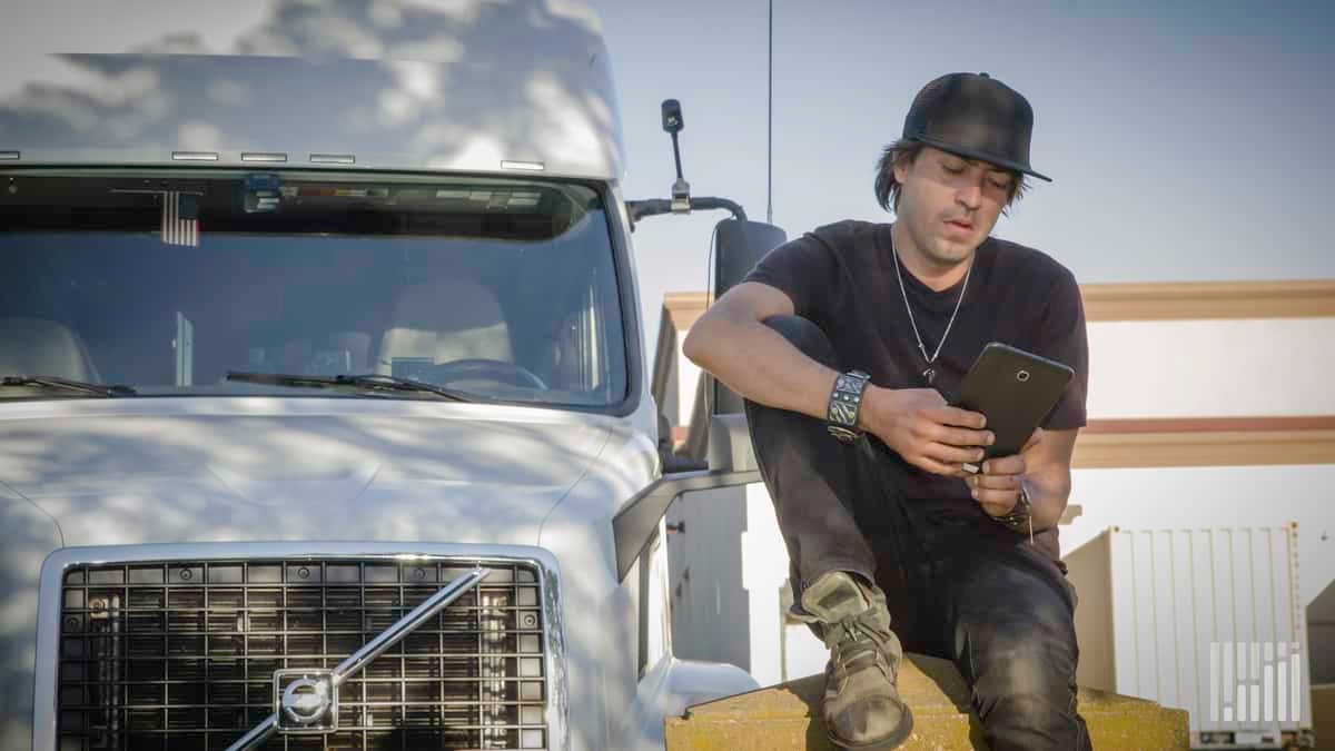 Driver leaning on his truck while using his tablet.