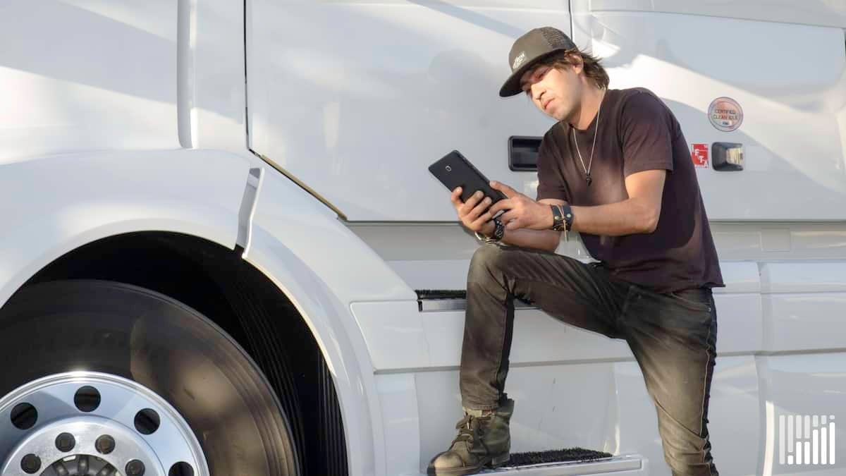 Driver leaning on his truck while using his tablet.