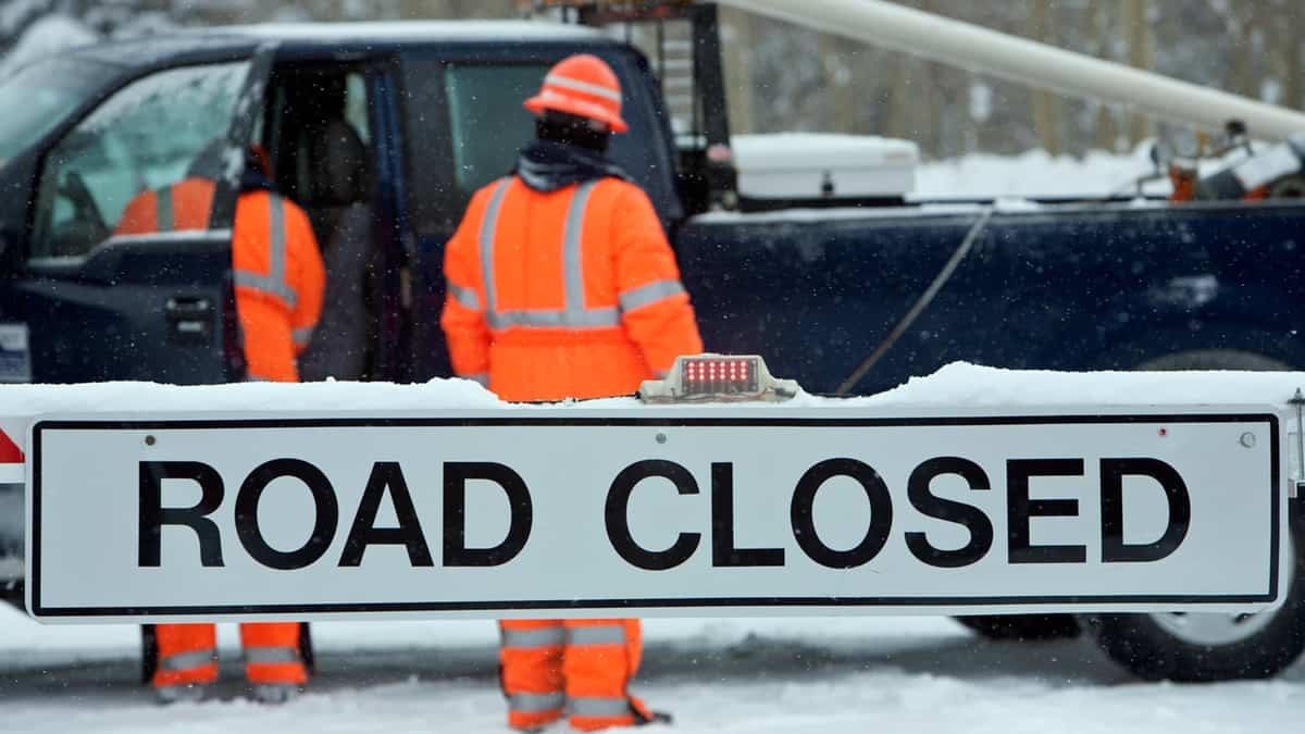 Crew placing "Road Closed" sign along a snowy road.