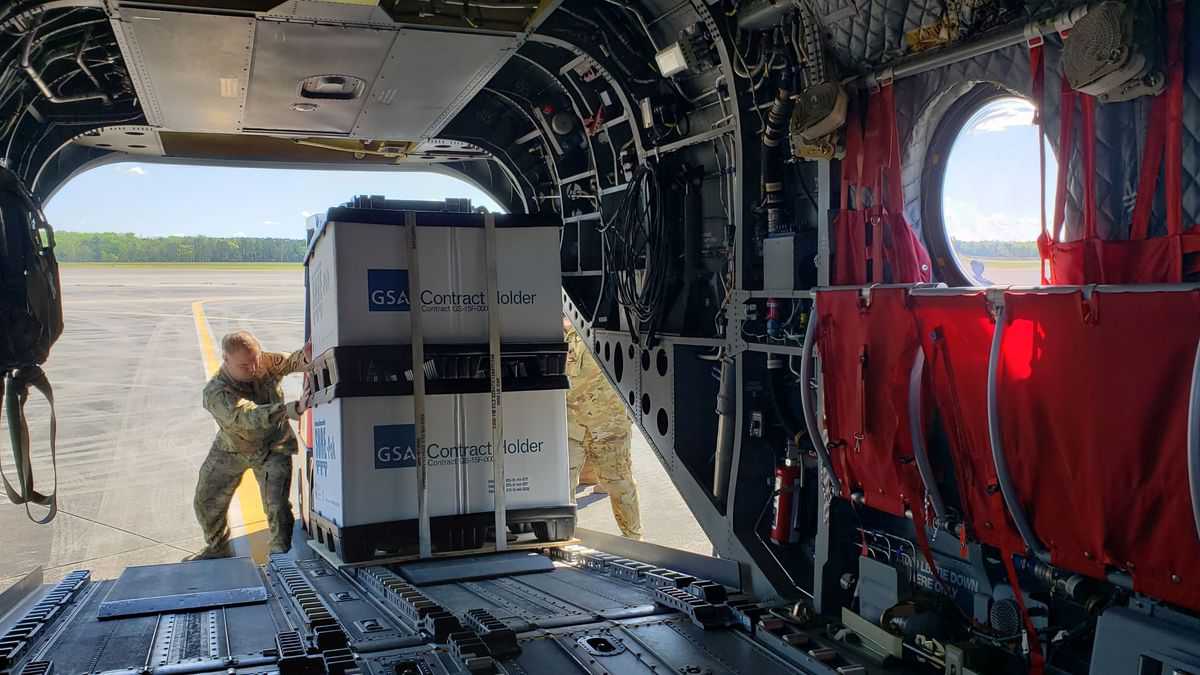 National Guard troops unload a large pallet out the back of a helicopter.