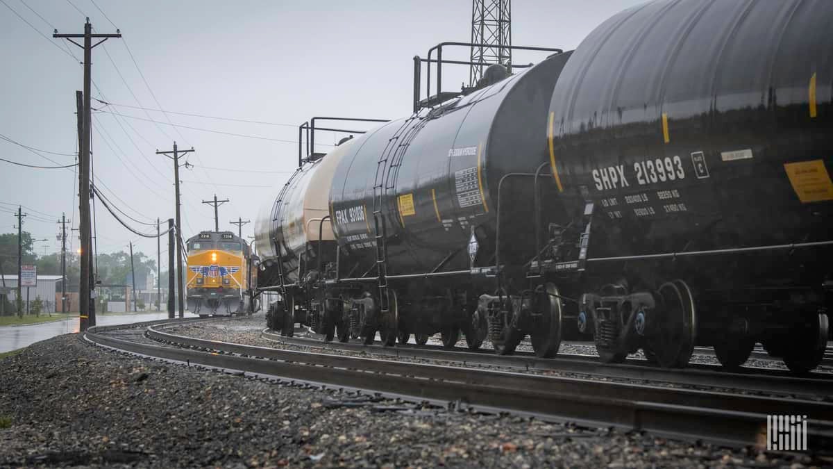 A photograph of a train with tank cars passing by a Union Pacific train.