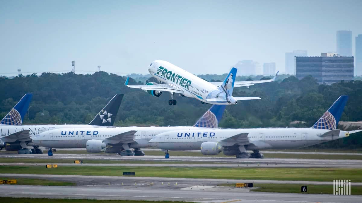 A white jet takes off with other planes sitting in the foreground and buildings from downtown Houston in the background.