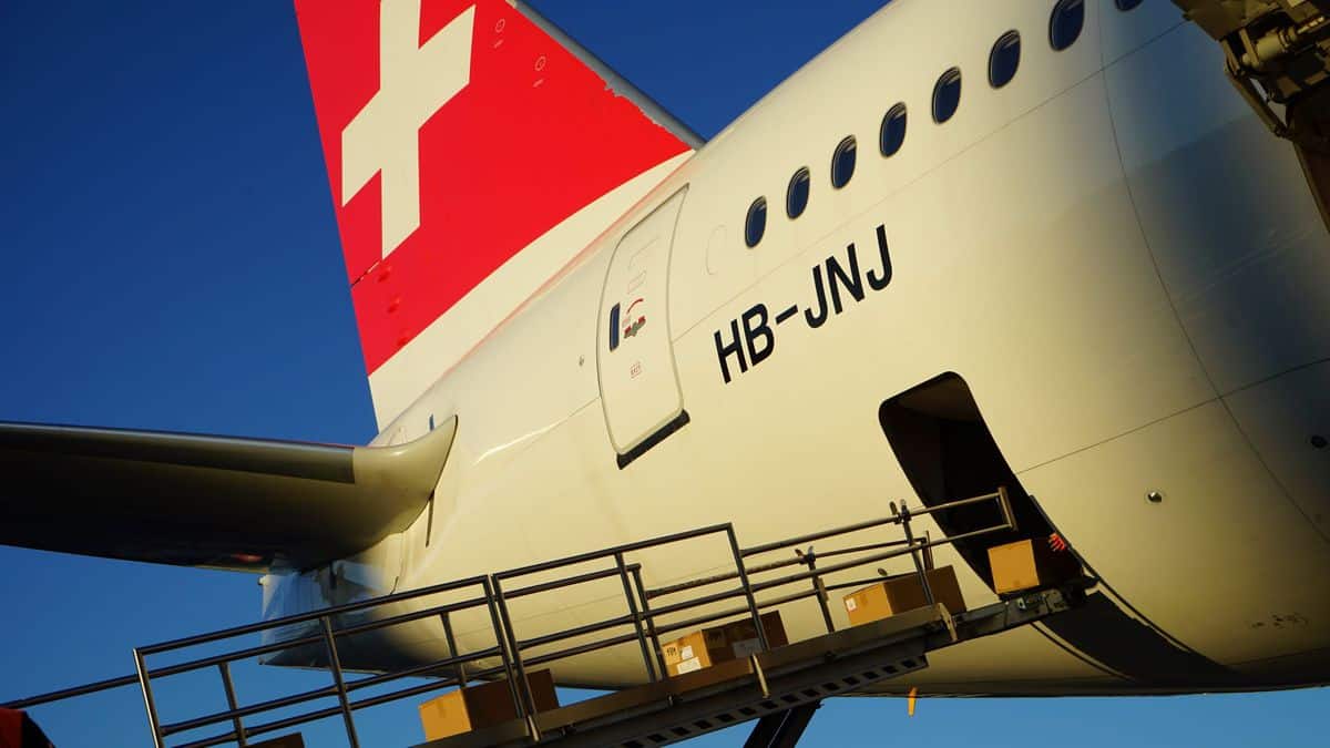 Boxes on a conveyor going up to the loading door of a Swiss International Air Lines' jet with a white cross painted on red tail.