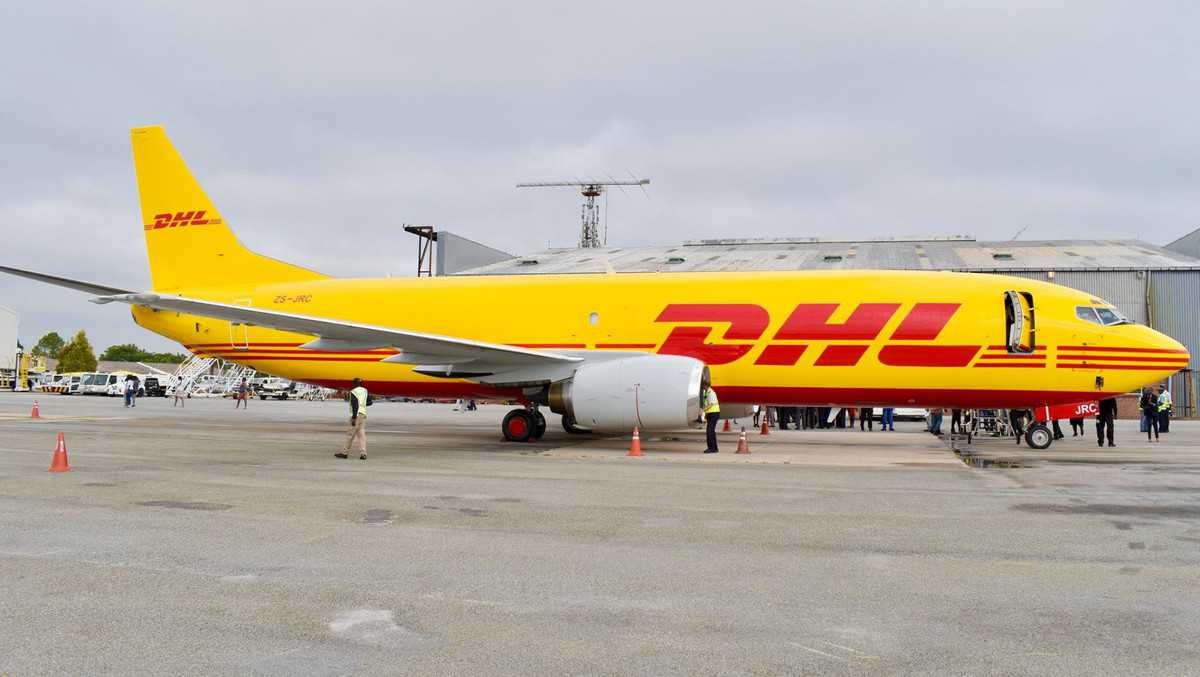 Mustard-yellow DHL freighter jet sitting at airport.