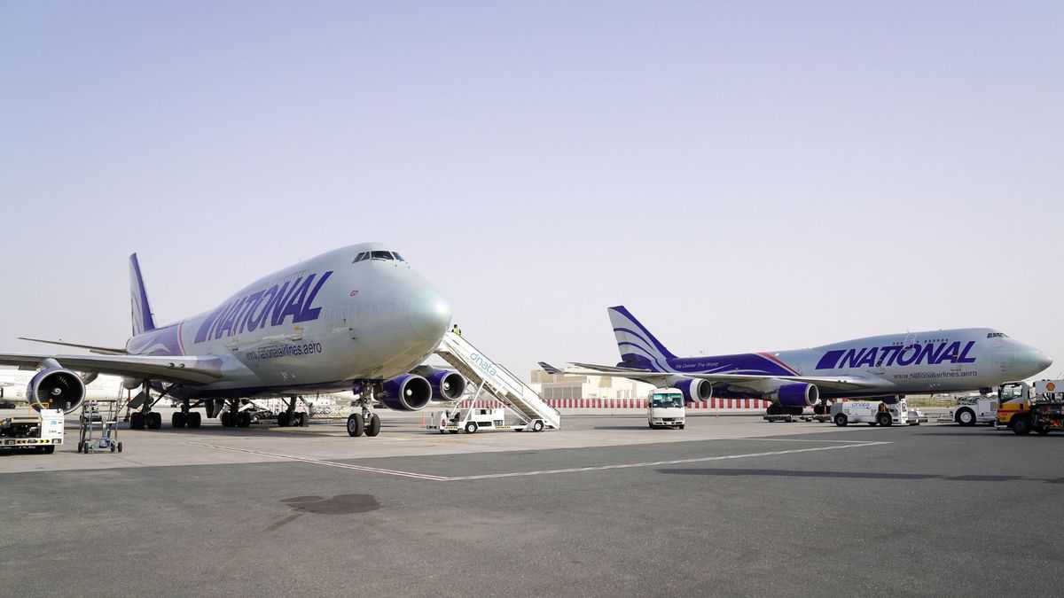 Two white 747 jumbo jets with blue lettering parked at airport, with stairs to front door.