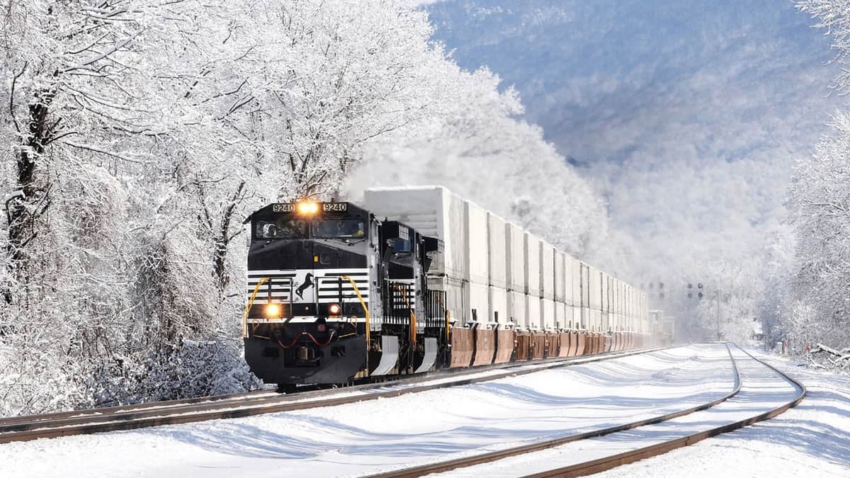 A photograph of a Norfolk Southern train traveling through a snowy landscape.