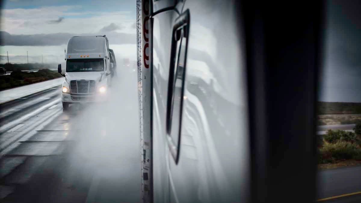 Tractor-trailers heading down highway on a rainy day.