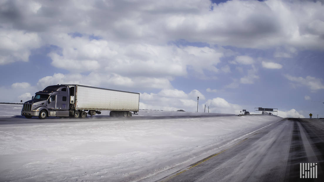 Tractor-trailer heading down snowy highway.