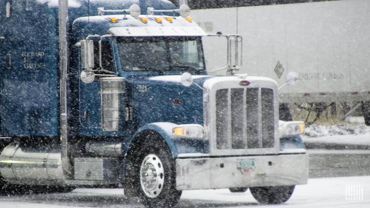 Tractor-trailer heading through snowfall.