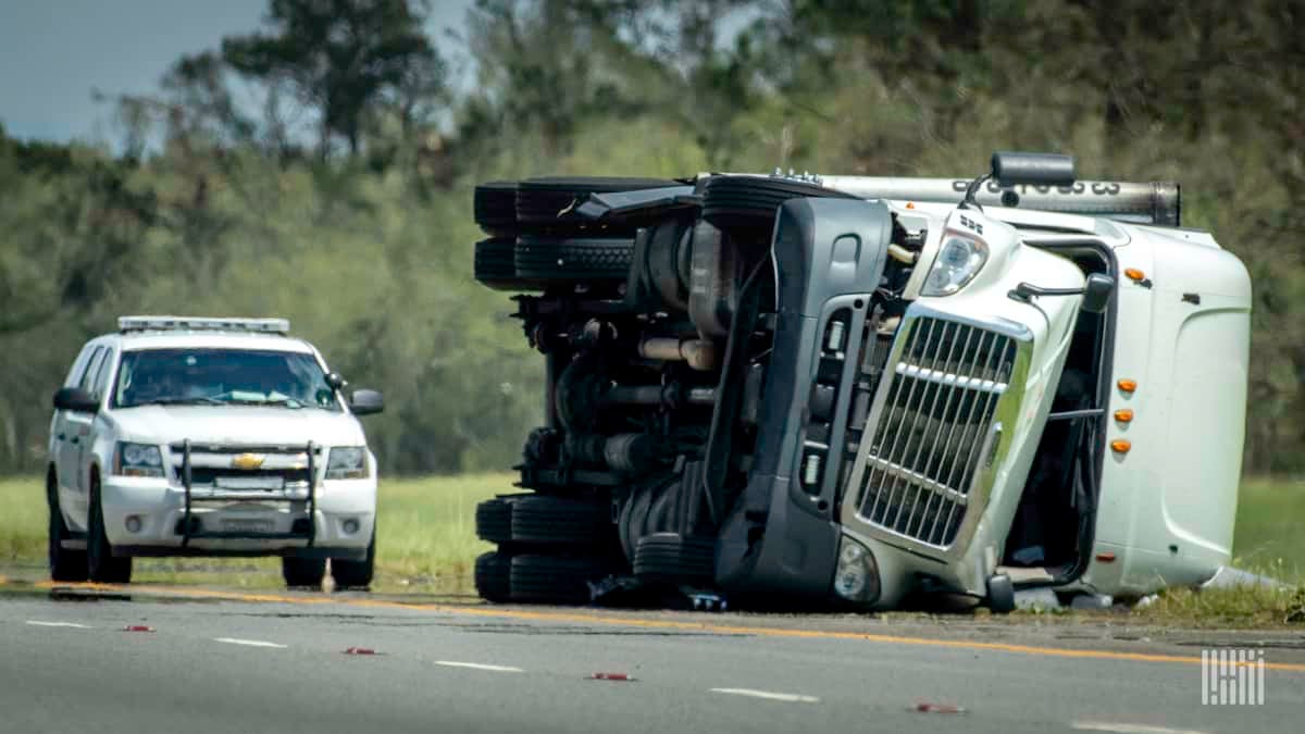 Flipped tractor-trailer on the side of a road.