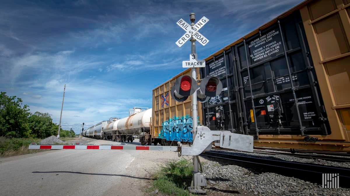 A photograph of a train passing by a rail crossing.