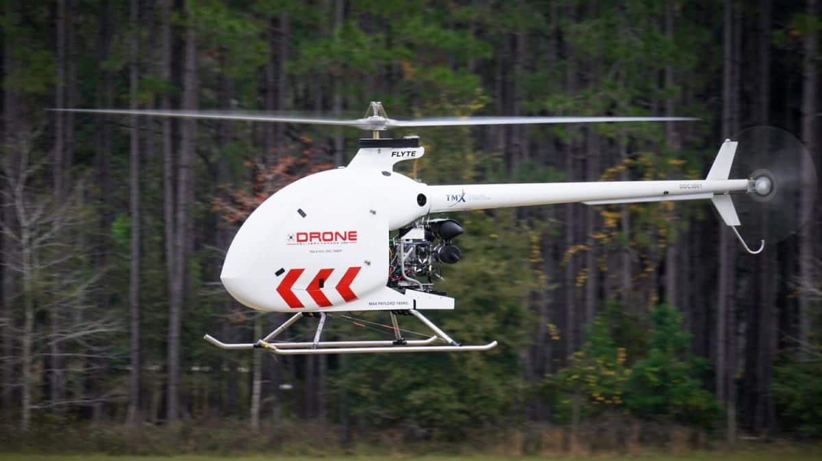 A white drone that looks like a helicopter flying with trees in background.