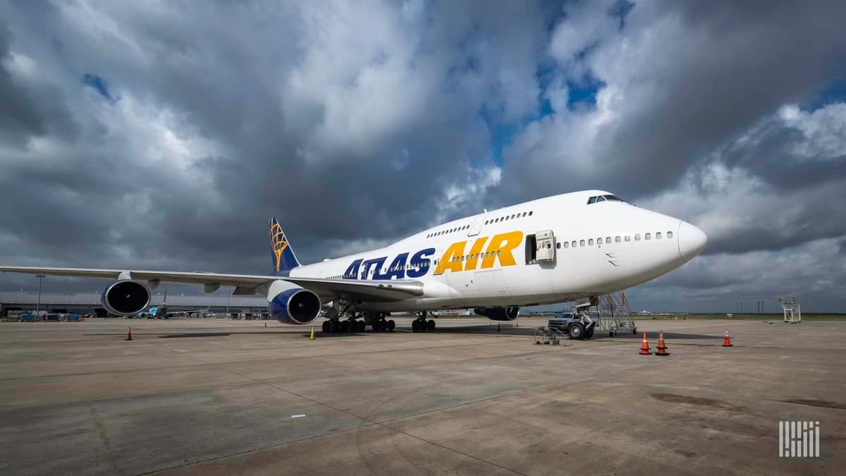 A white Atlas Air jumbo cargo jet on tarmac with dark skies over it.