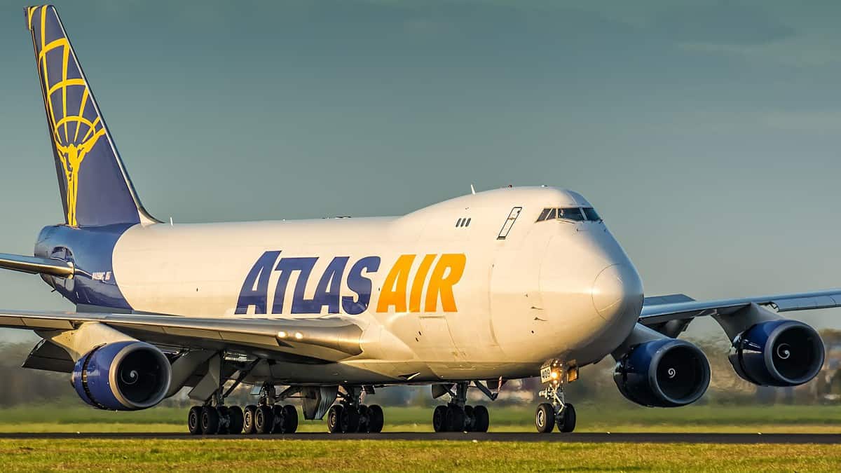 A white jumbo jet with Atlas Air name and blue tail painted on it. on sunny day rolls down airport roadway.