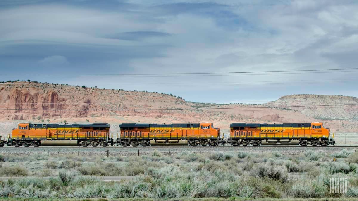 A photograph of a BNSF train passing by a desert mountain.