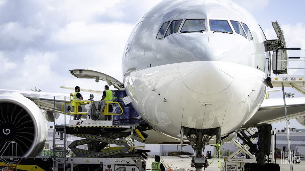 Looking straight at nose of cargo jet, painted gray on top half, white on bottom, with side cargo door open and loading a container of freight.