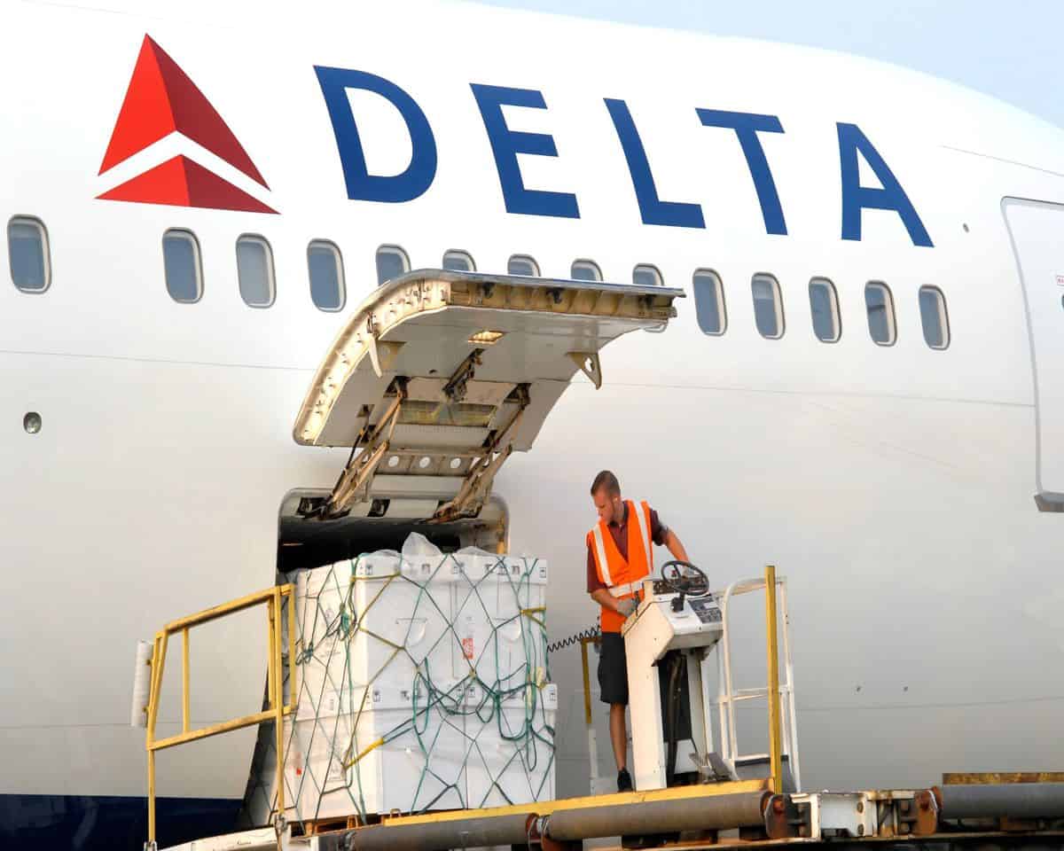 A pallet of cargo on a hydraulic lift gets moved into the side door of a white Delta Air Lines airplane.