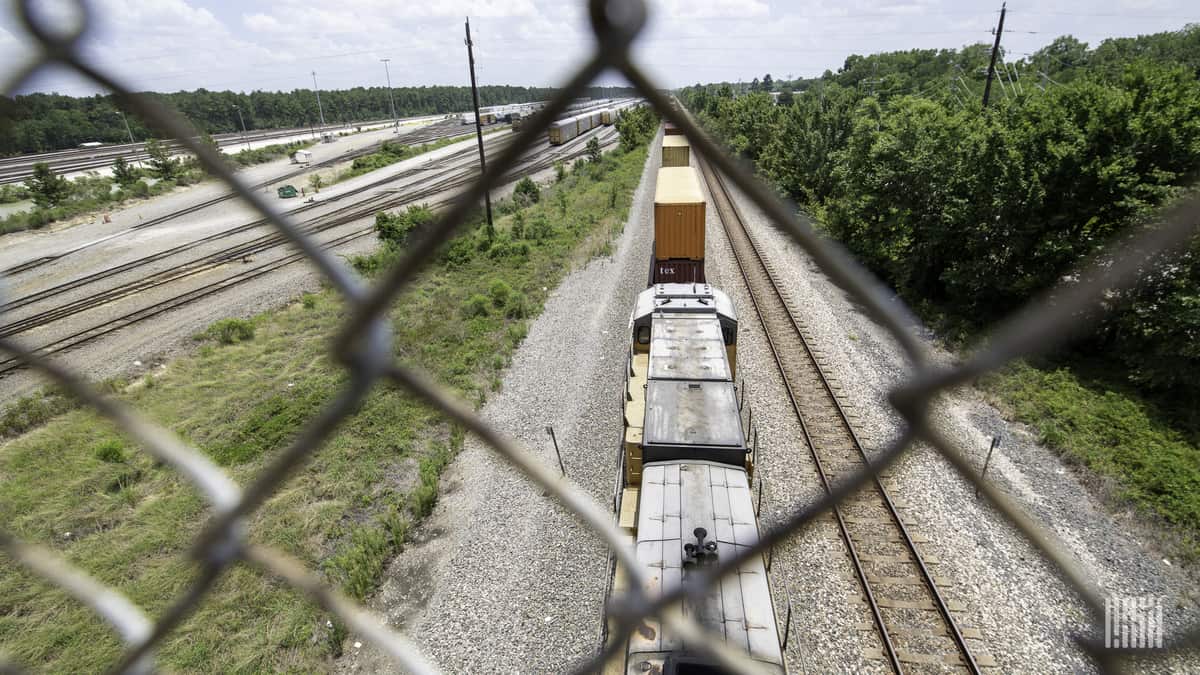 A photograph of a train traveling next to a highway.