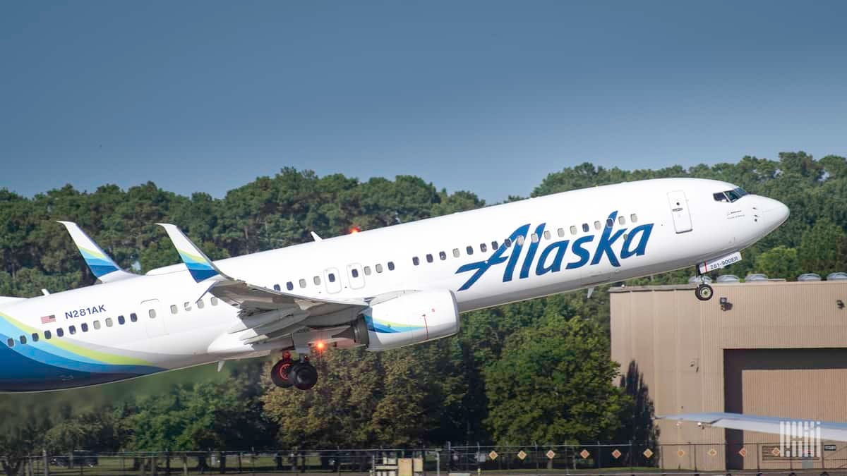 A white Alaska Airlines jet coming in for a landing with wheels down, about to touch down on runway on sunny day.