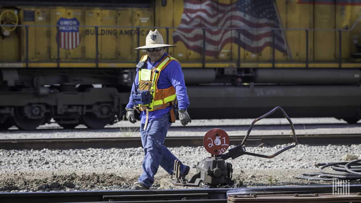 A photograph of a man inspecting track at a rail yard.