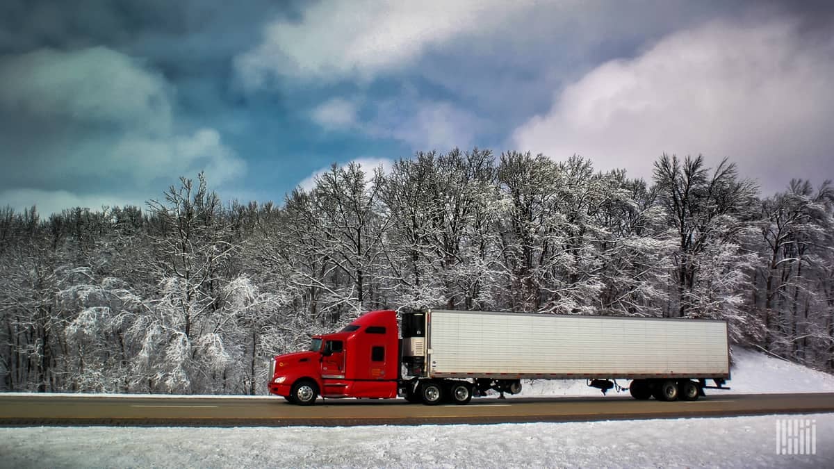 Reefer truck heading down highway with snow in the surrounding mountains and grass.