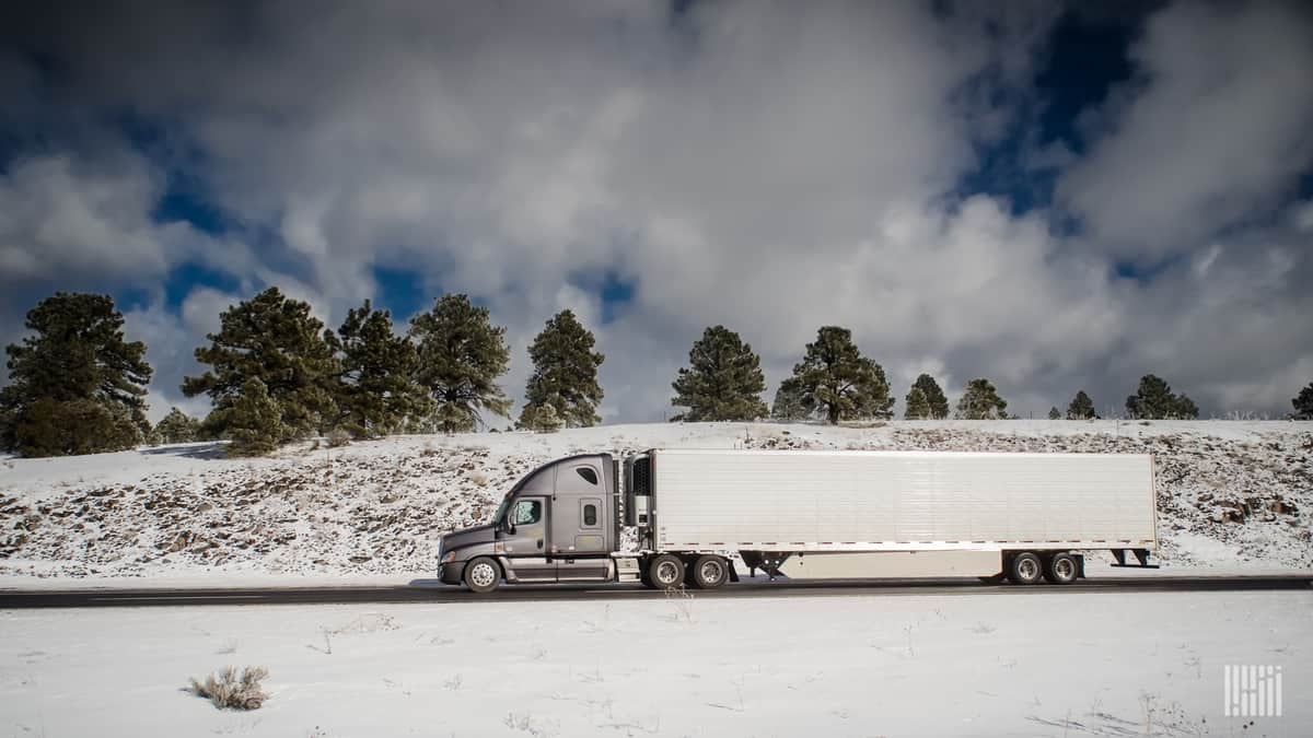 Reefer tractor-trailer heading down highway with snow-covered hills.