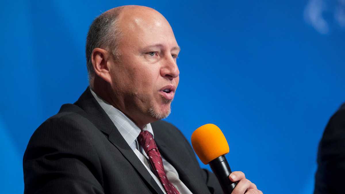 White man with receding hair speaking into handheld microphone at conference.