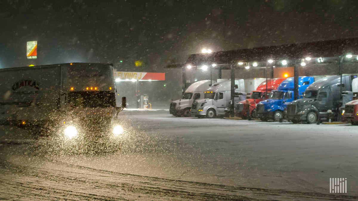 Tractor-trailers at a truck stop on a snowy night.