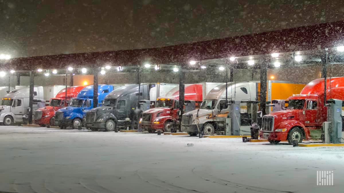 Tractor-trailers parked at a truck stop on a snowy night.