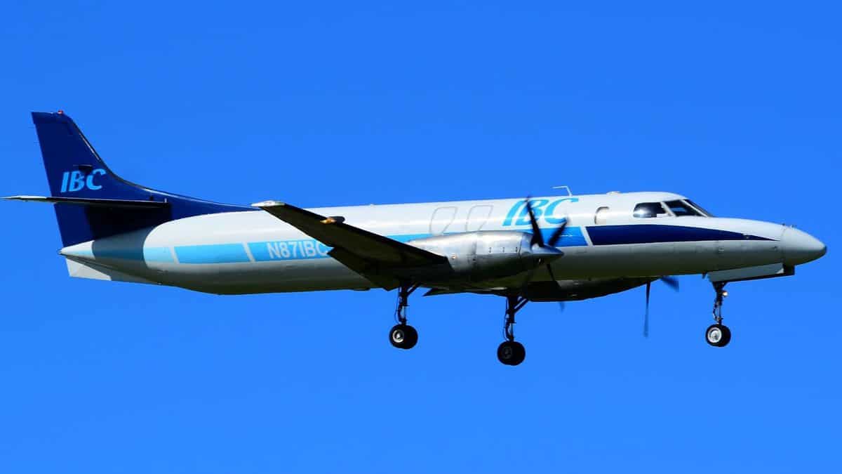 A small propeller-driven cargo plane comes in for landing with wheels down against bright blue sky.