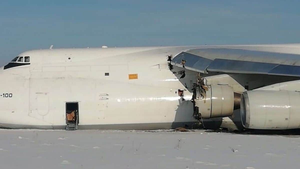 A big white freighter aircraft lies in snow at end of runway with damaged engine after emergency landing.