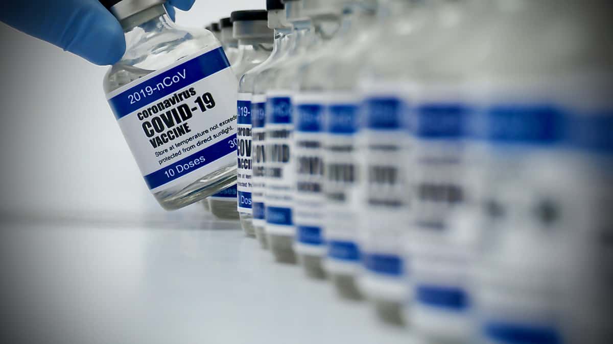 A gloved-hand reaches for vial of a COVID-19 vaccine dose. The distribution of COVID-19 vaccines could begin in mid-December