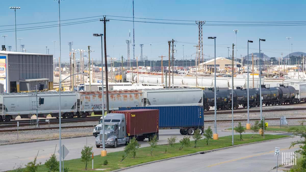 A photograph of a truck passing by a rail yard.