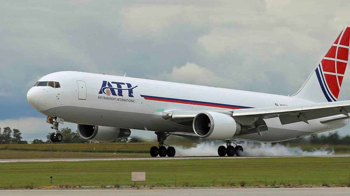 A large white plane with red tail touches down on runway. ATI is lettering.